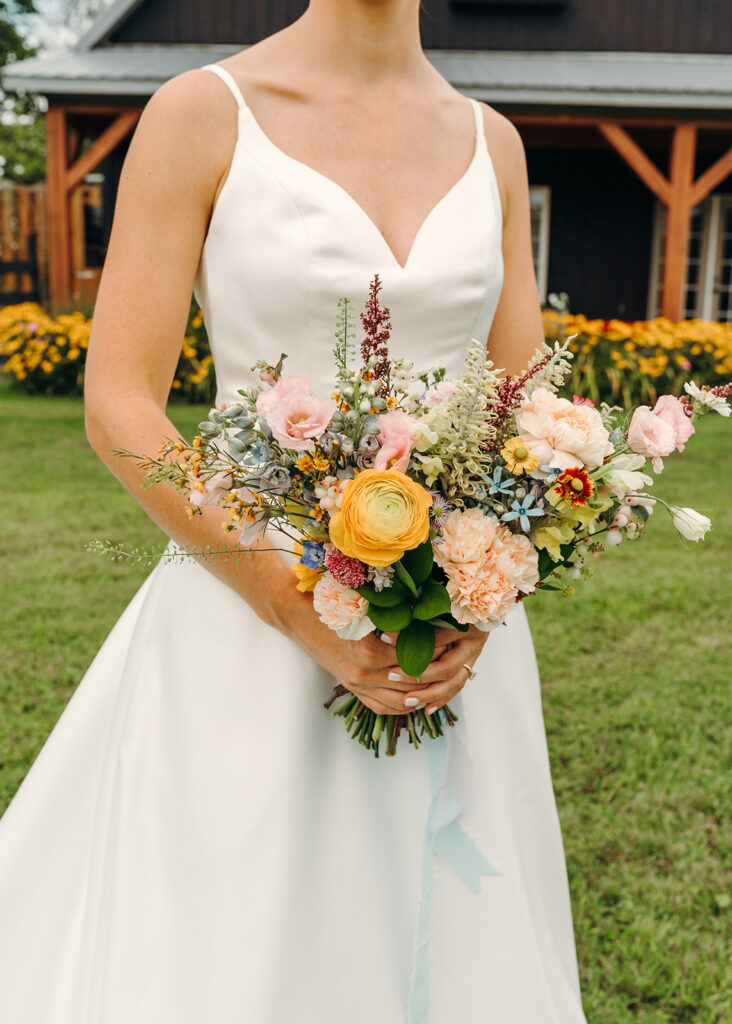 A bride carrying a garden-style bridal bouquet of multi-colored flowers by Refined Gatherings